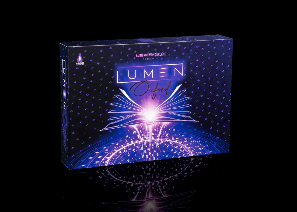 A boxed product labeled 'LUMEN Oxford' stands upright on a glossy black surface against a black background. The box art is predominantly dark blue and purple with a bright glowing white and pink burst at the center and small dotted star-like patterns across the surface.